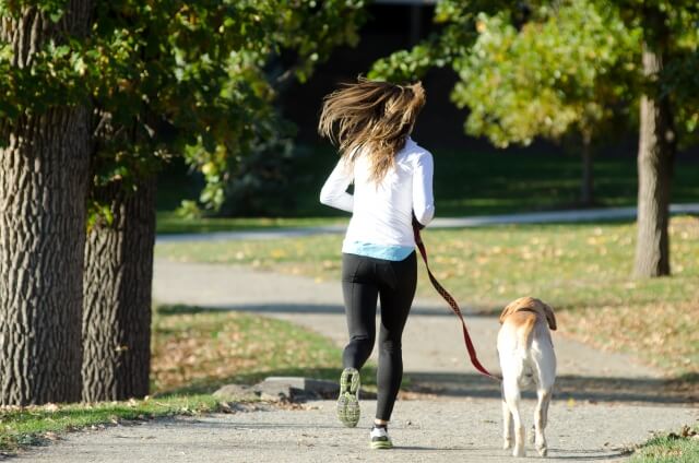 犬を散歩させながらランニングしている女性